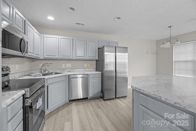 kitchen featuring a sink, appliances with stainless steel finishes, gray cabinets, light wood finished floors, and decorative light fixtures