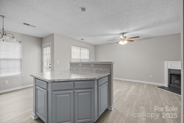 kitchen with visible vents, a kitchen island, decorative light fixtures, light countertops, and a fireplace