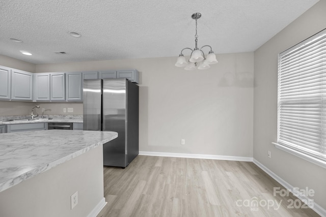 kitchen featuring decorative light fixtures, gray cabinets, light countertops, freestanding refrigerator, and a sink