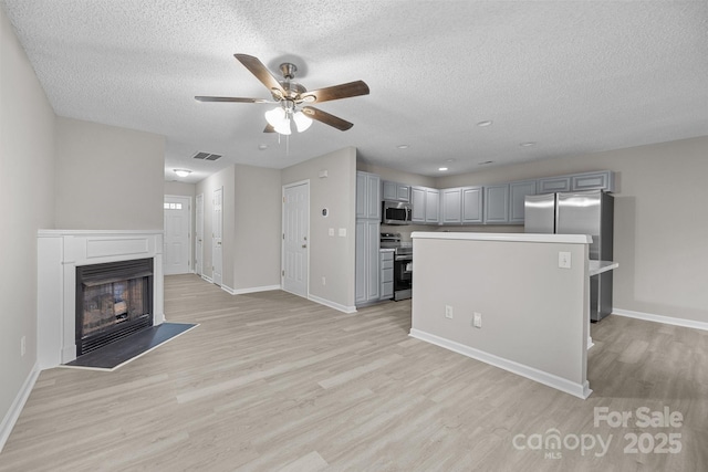 unfurnished living room with light wood-type flooring, a fireplace, visible vents, and baseboards