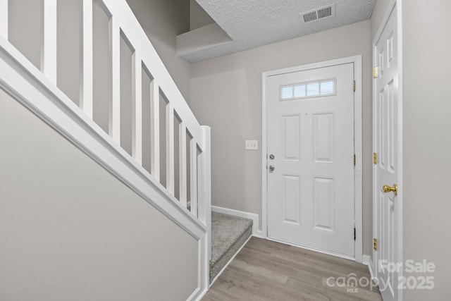 foyer entrance with baseboards, visible vents, light wood-style flooring, stairs, and a textured ceiling