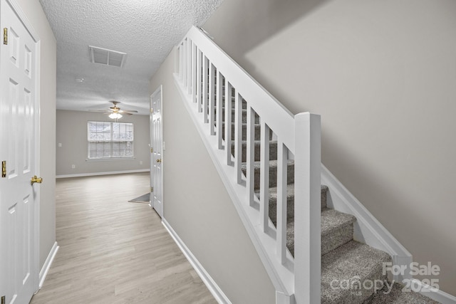 stairway featuring baseboards, a textured ceiling, visible vents, and wood finished floors