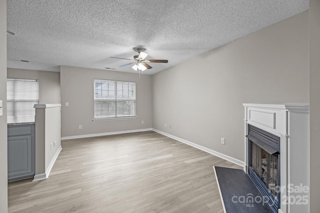 unfurnished living room with baseboards, a fireplace with raised hearth, ceiling fan, and light wood finished floors