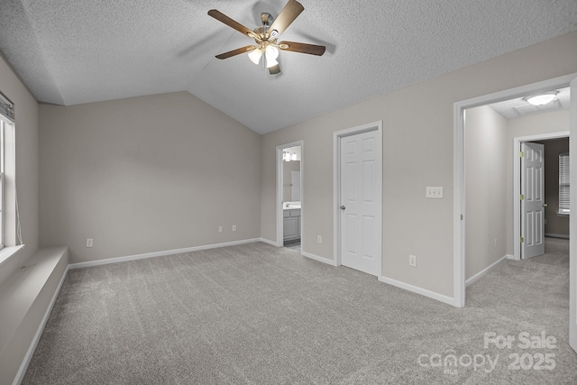 unfurnished bedroom with a textured ceiling, ensuite bathroom, light carpet, baseboards, and vaulted ceiling