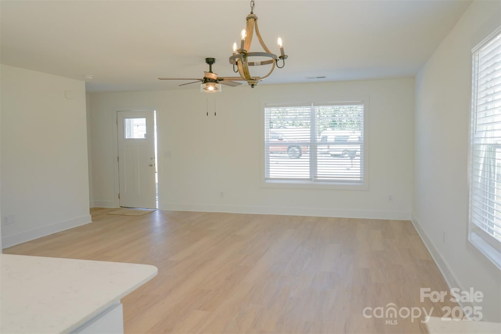 interior space with ceiling fan with notable chandelier and light hardwood / wood-style flooring