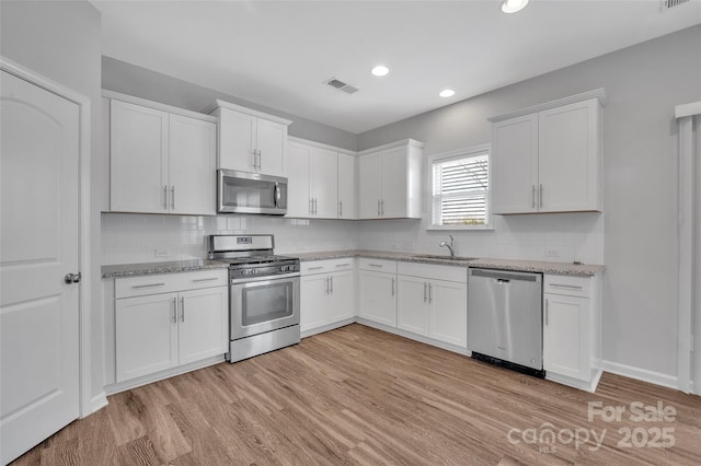 kitchen featuring white cabinetry, appliances with stainless steel finishes, sink, and light stone counters