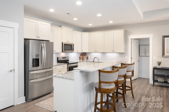 kitchen with hardwood / wood-style flooring, stainless steel appliances, light stone counters, a kitchen bar, and decorative backsplash