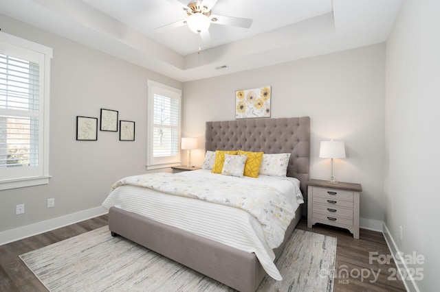 bedroom with dark hardwood / wood-style floors, ceiling fan, and a raised ceiling