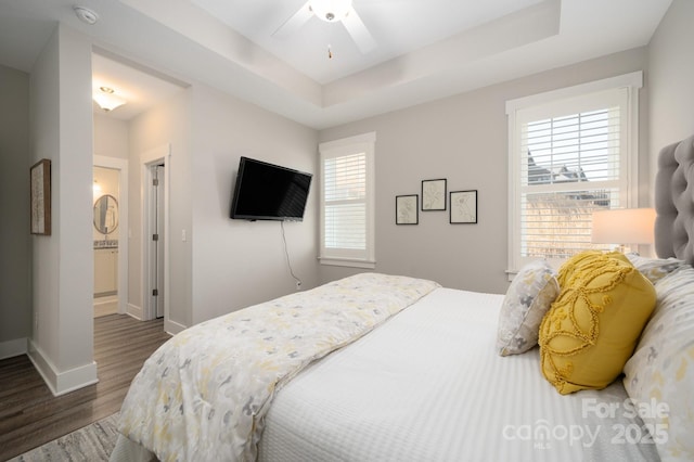 bedroom with a tray ceiling, ceiling fan, dark hardwood / wood-style flooring, and ensuite bath