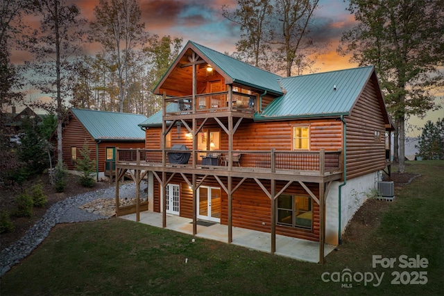 back house at dusk with a patio, a yard, a deck, and a balcony