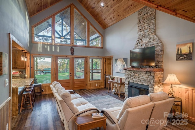 living room featuring high vaulted ceiling, dark wood-type flooring, wood ceiling, and a stone fireplace