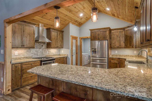 kitchen with sink, pendant lighting, stainless steel appliances, wall chimney exhaust hood, and kitchen peninsula