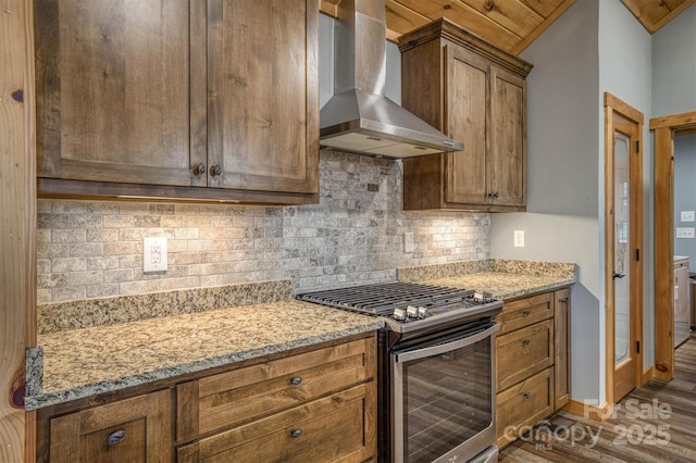 kitchen featuring wall chimney exhaust hood, dark hardwood / wood-style flooring, light stone countertops, stainless steel gas stove, and decorative backsplash