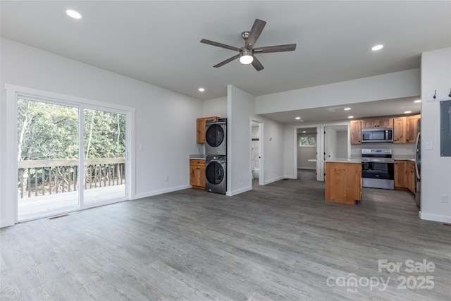 unfurnished living room with recessed lighting, stacked washer and clothes dryer, baseboards, and wood finished floors