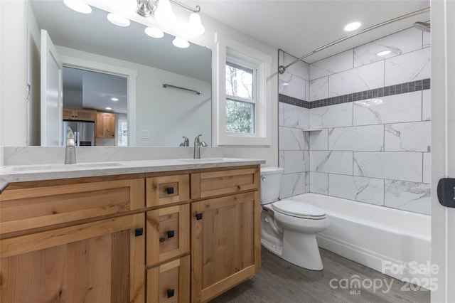 full bathroom with toilet, double vanity, a sink, and wood finished floors