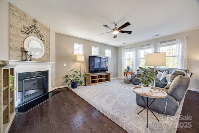 living area featuring a glass covered fireplace, a healthy amount of sunlight, visible vents, and wood finished floors