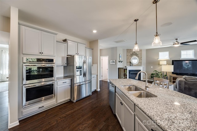 kitchen featuring a sink, open floor plan, appliances with stainless steel finishes, a glass covered fireplace, and pendant lighting