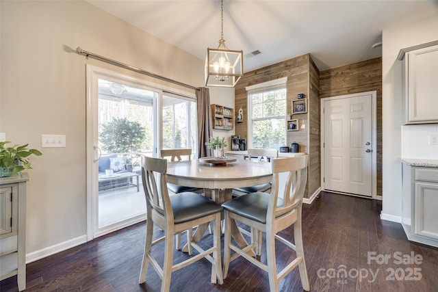 dining area featuring a chandelier, wooden walls, dark wood finished floors, and baseboards