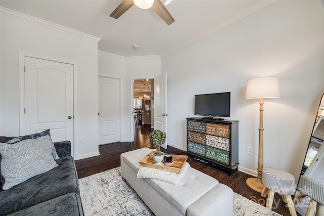 living room featuring dark wood-type flooring, crown molding, baseboards, and ceiling fan