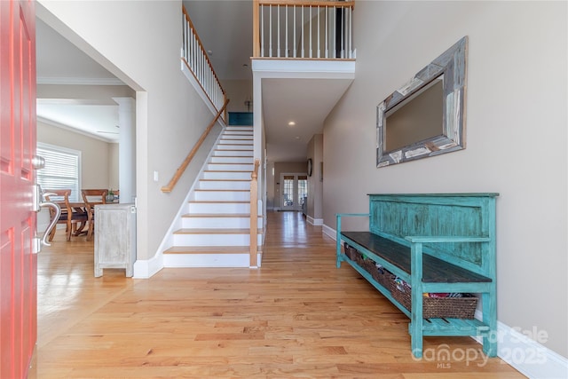 entrance foyer with ornamental molding, light wood-type flooring, and a high ceiling