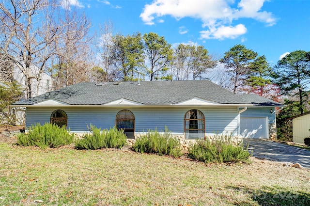 ranch-style home with a garage, a front yard, roof with shingles, and driveway