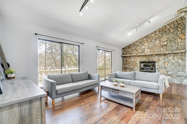 living area with a ceiling fan, lofted ceiling, wood-type flooring, and a stone fireplace