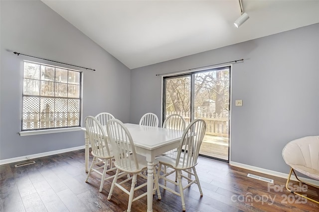 dining space featuring dark wood finished floors, visible vents, vaulted ceiling, and baseboards