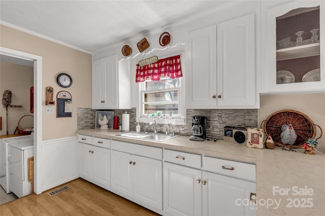 kitchen with a sink, white cabinetry, washer and dryer, light countertops, and glass insert cabinets