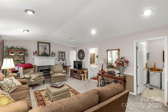 living room featuring a fireplace, vaulted ceiling, and light colored carpet