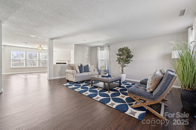 living room featuring visible vents, a textured ceiling, baseboards, and wood finished floors