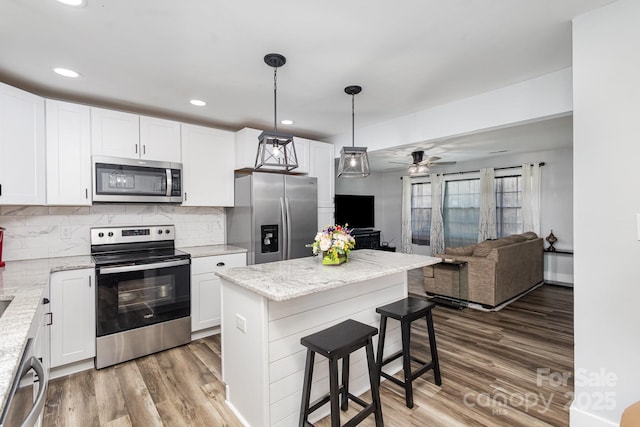 kitchen with light stone counters, appliances with stainless steel finishes, open floor plan, white cabinetry, and a kitchen breakfast bar