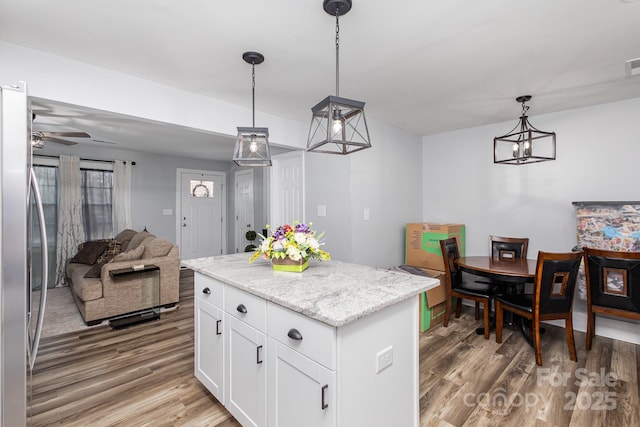 kitchen featuring open floor plan, hanging light fixtures, stainless steel refrigerator, and white cabinets