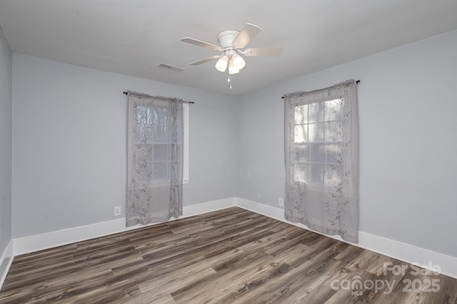 empty room featuring ceiling fan, dark wood finished floors, visible vents, and baseboards