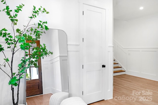 entryway featuring a decorative wall, stairway, light wood-style floors, and wainscoting