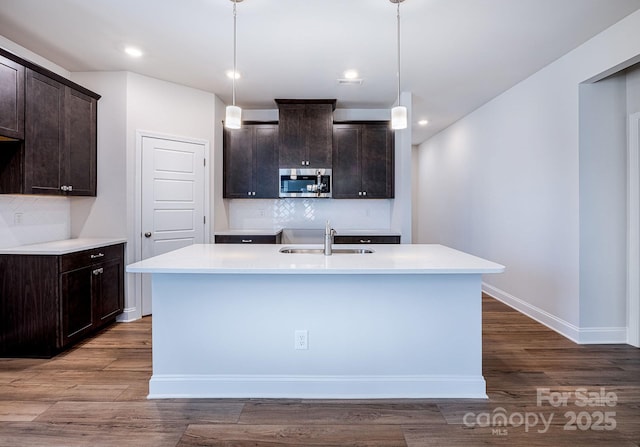 kitchen featuring sink, a kitchen island with sink, dark brown cabinetry, and decorative light fixtures