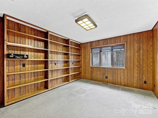 carpeted spare room featuring a textured ceiling and wood walls