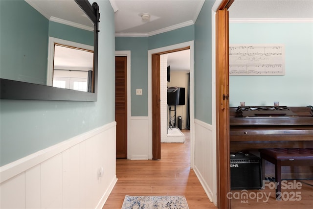 hall featuring light wood-type flooring, a wainscoted wall, and ornamental molding