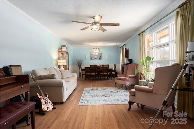 living area featuring light wood-style floors, a ceiling fan, and crown molding