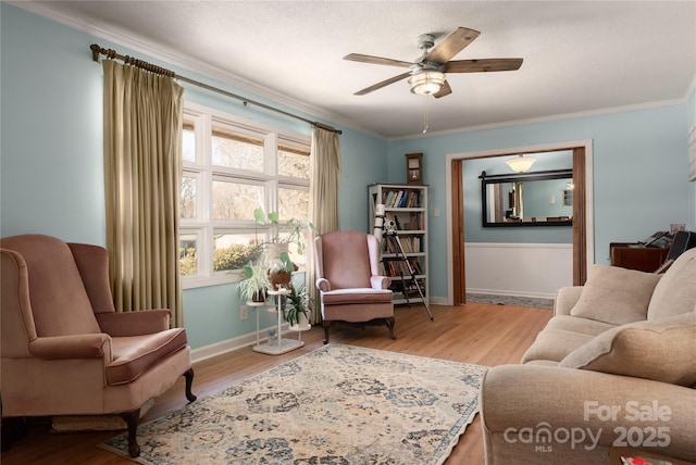 living area featuring a ceiling fan, crown molding, baseboards, and wood finished floors