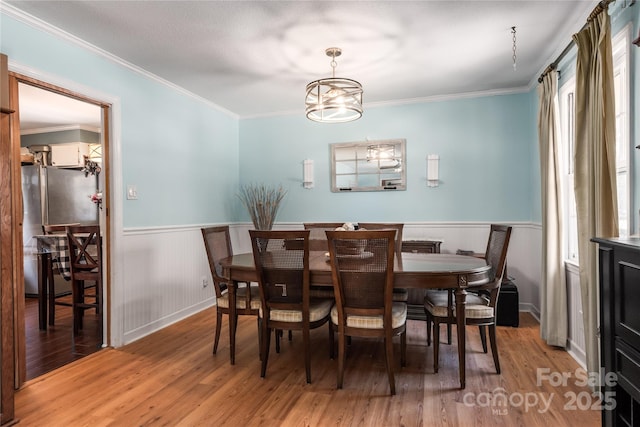 dining area featuring ornamental molding, wainscoting, a notable chandelier, and wood finished floors