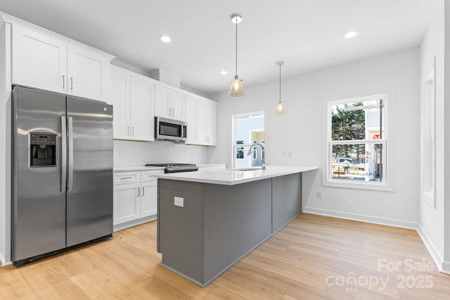 kitchen featuring appliances with stainless steel finishes, light hardwood / wood-style flooring, pendant lighting, backsplash, and white cabinetry