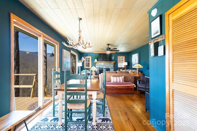dining space featuring wood-type flooring, a fireplace, and ceiling fan with notable chandelier
