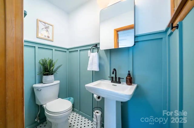 bathroom featuring a decorative wall, toilet, a wainscoted wall, and a sink