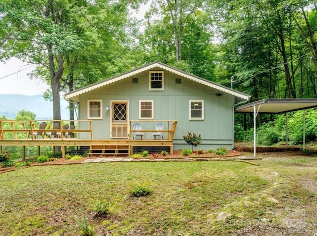 rear view of property with a detached carport, board and batten siding, a yard, and a wooden deck