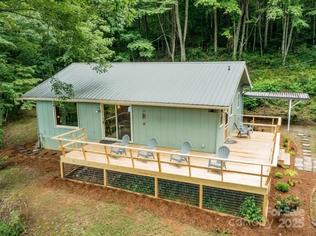back of house with a wooded view, metal roof, and a wooden deck