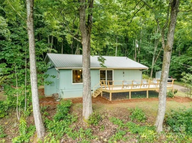 back of property featuring a view of trees, metal roof, and a wooden deck