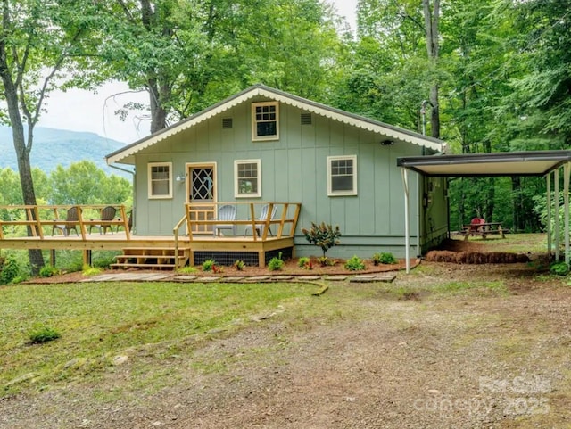 back of house with board and batten siding, a wooden deck, and a lawn