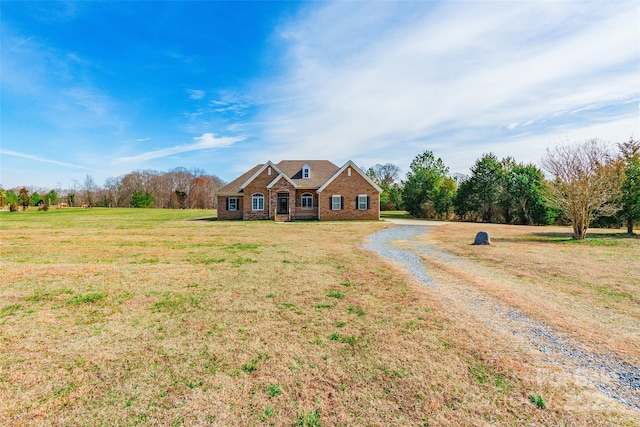 view of front of home featuring driveway, brick siding, a rural view, and a front yard