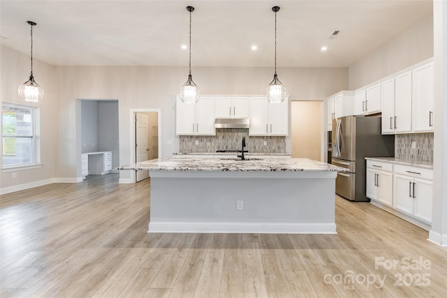 kitchen featuring under cabinet range hood, a center island with sink, and white cabinets