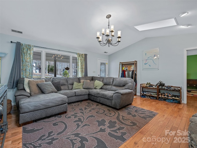 living room with light wood-style floors, vaulted ceiling with skylight, a chandelier, and visible vents